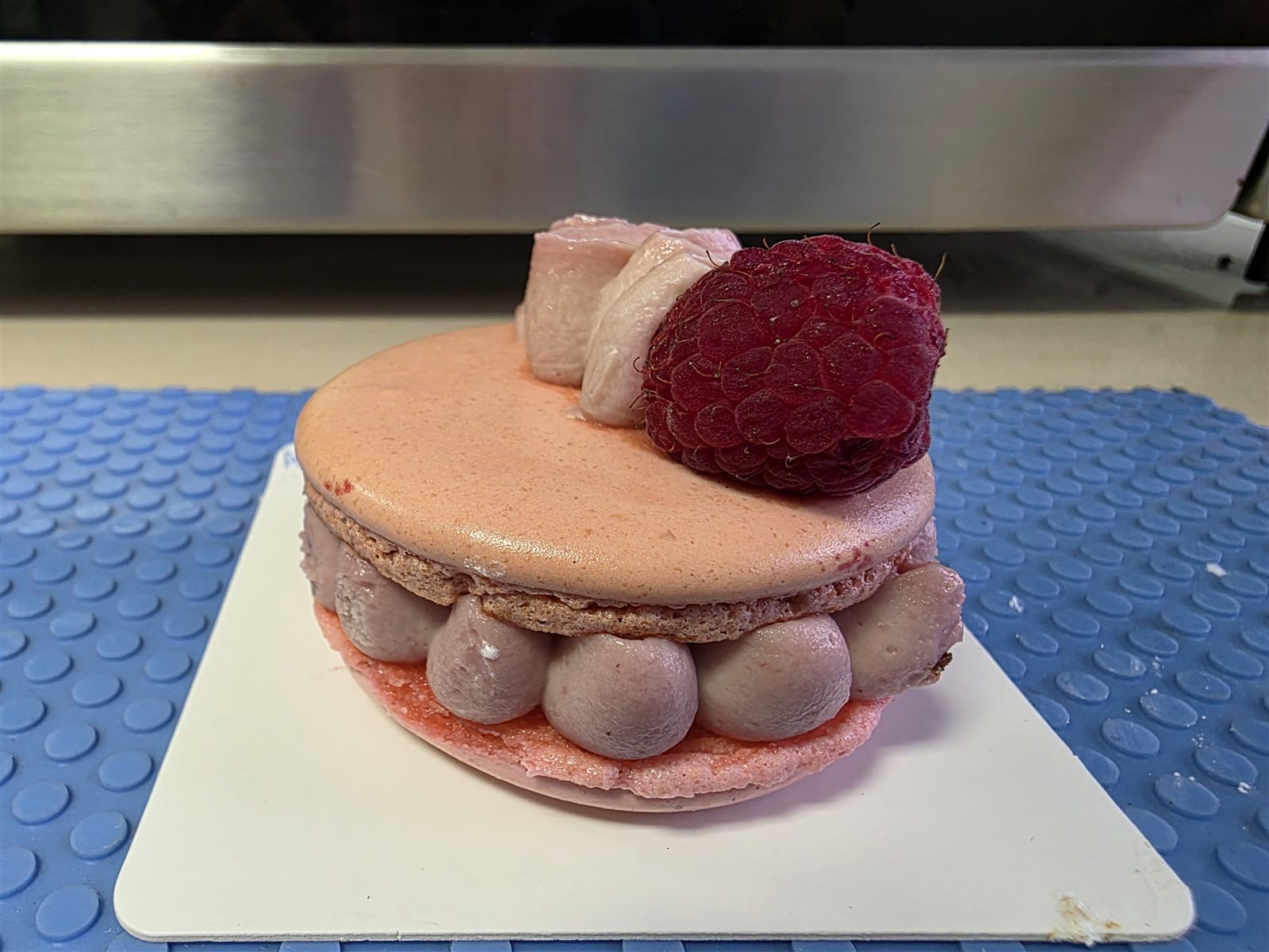 Pink raspberry macaron filled with piped cream and topped with a fresh raspberry