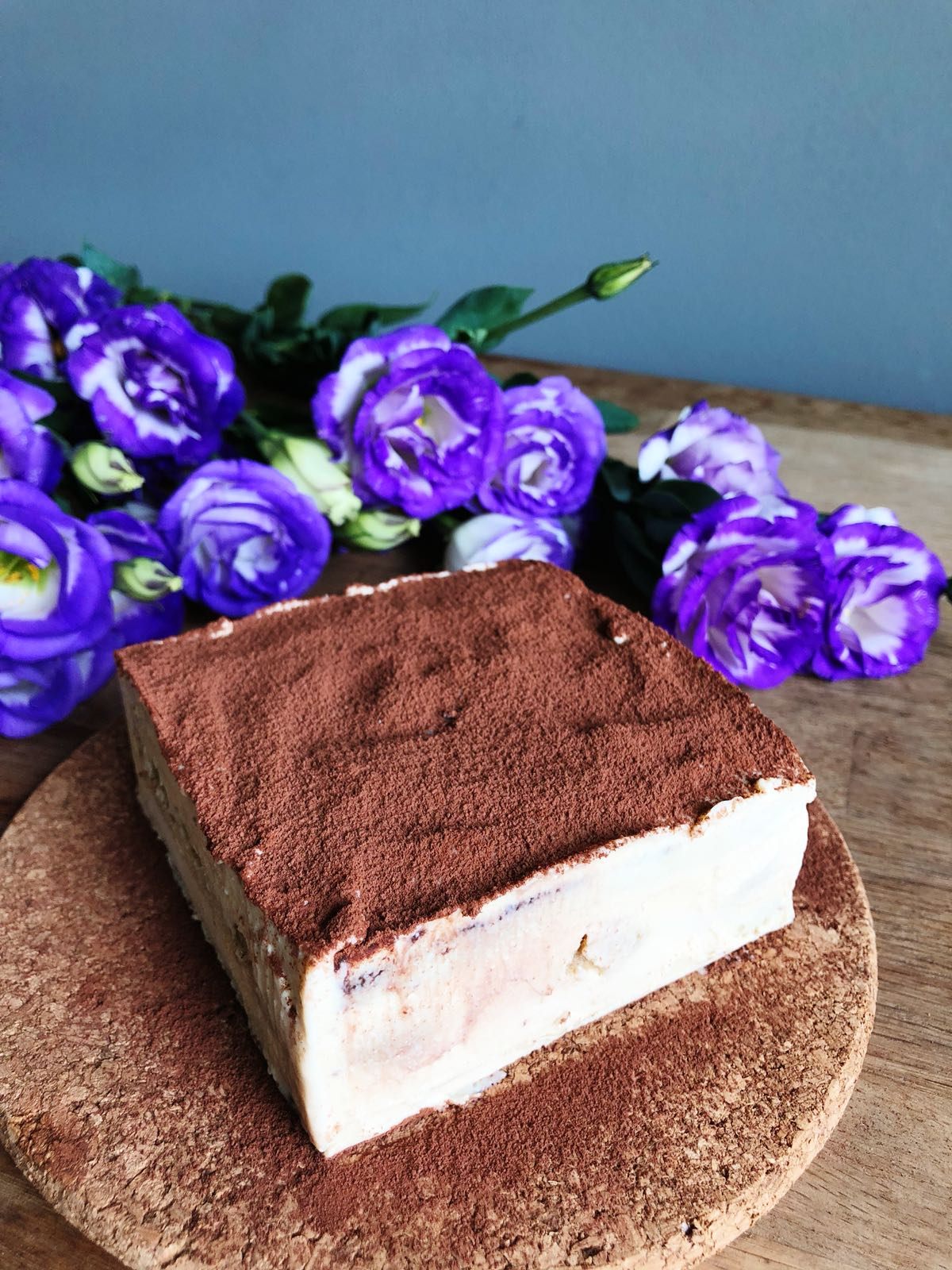 Gluten-free tiramisu dusted with cocoa, beside purple lisianthus flowers